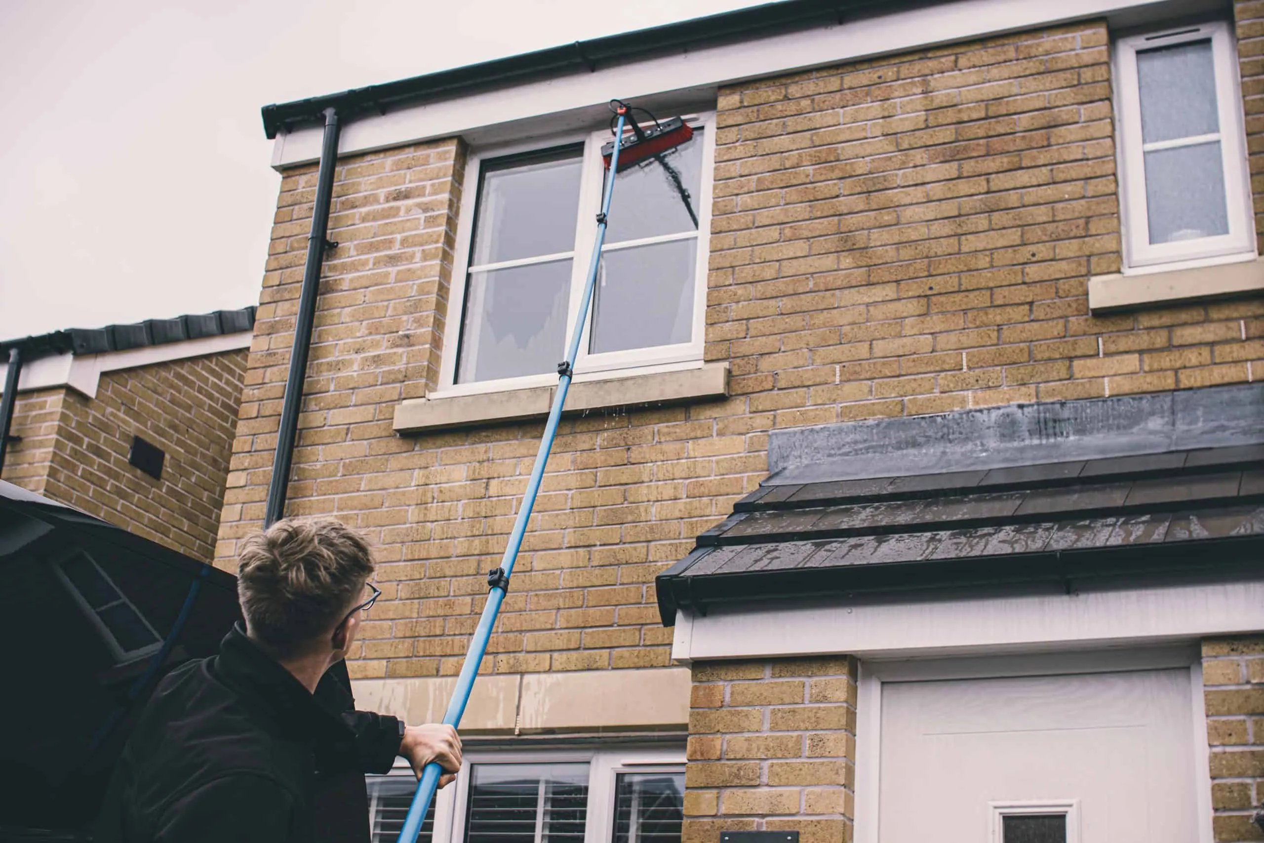 Professional window cleaning using extension pole on a residential house.
